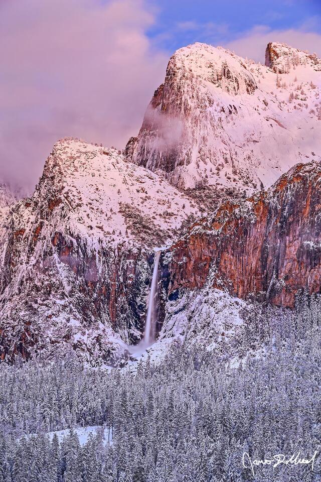 Alpenglow lights the clouds & snow covered tops of Cathedral Rocks and Spires with a faint magenta glow, as Bridalveil Fall tumbles over the snow covered cliffs