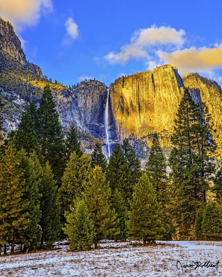 Yosemite Falls plummets towards the Yosemite Valley floor in the late autumn as golden hour light illuminates the granite cliffs while snow covers the valley.