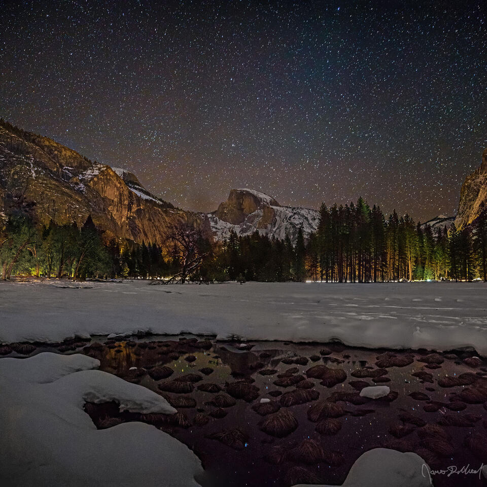 The night sky shines brightly over snow covered Cook's Meadow in Yosemite Valley as Half Dome rises high above, reflecting in an ephemeral pool of water.