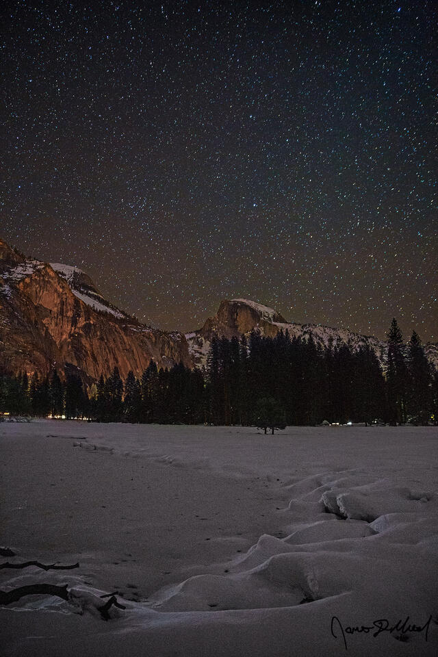 The night sky shines brightly over snow covered Cook's Meadow in Yosemite Valley as Half Dome rises high above the snow covered meadow.