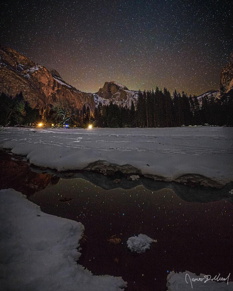 The night sky shines brightly over snow covered Cook's Meadow in Yosemite Valley as Half Dome rises high above, reflecting in an ephemeral pool of water.