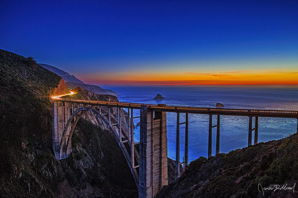 Nautical Sunset sets in over the Bixby Bridge and the Pacific Ocean as the last light of sunset fades away on the horizon while the stars begin to shine above.