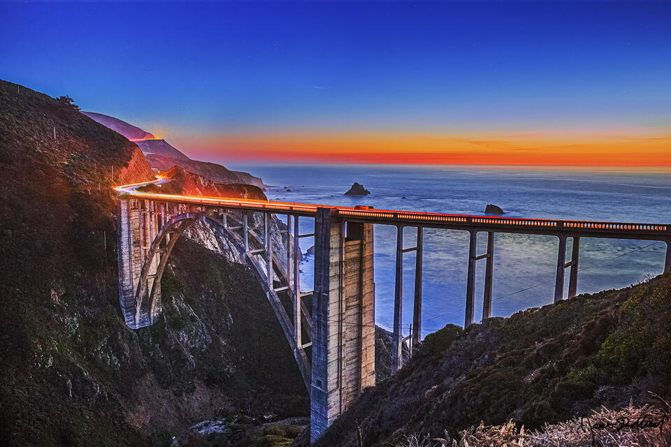 Nautical Sunset sets in over the Bixby Bridge and the Pacific Ocean as the last light of sunset fades away on the horizon while the stars begin to shine above.