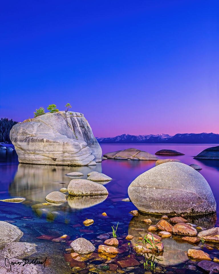 Long after sunset has passed, soft pastel alpenglow hangs on illuminating the skies above Lake Tahoe and Bonsai rock as dusk sets in over the mirror like water.