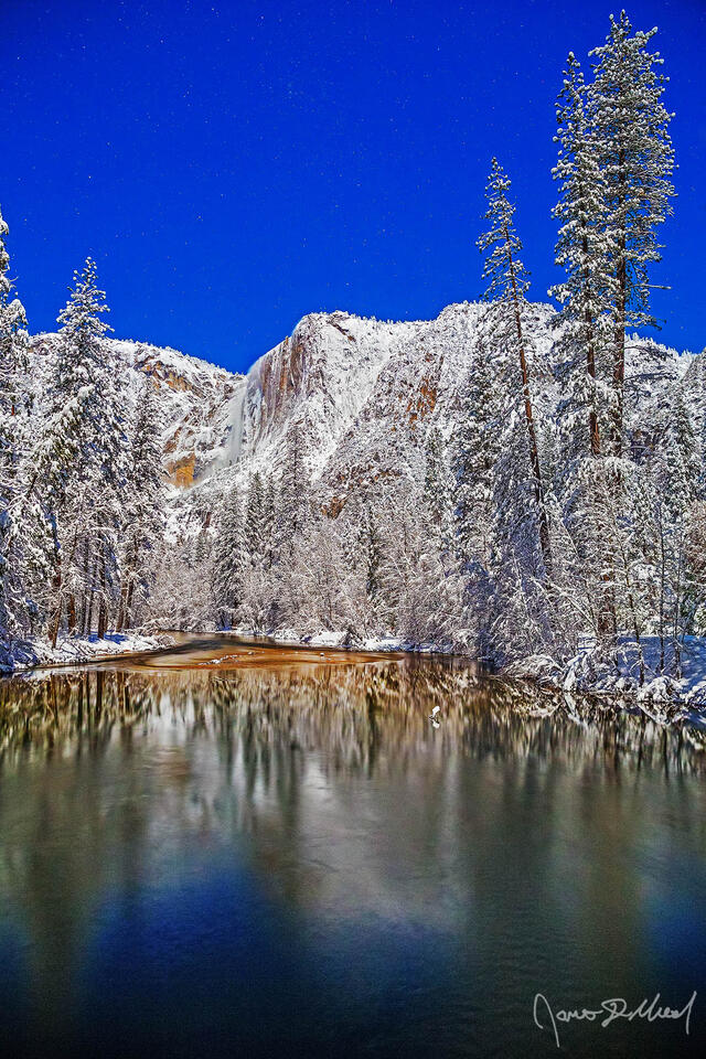 Moonlight illuminates Yosemite Falls as it tumbles 2425 feet over the snow covered granite cliffs above the Merced River and Yosemite Valley in the winter.
