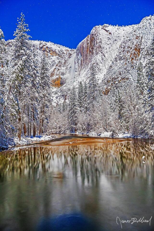 Moonlight illuminates Yosemite Falls as it tumbles 2425 feet over the snow covered granite cliffs above the Merced River and Yosemite Valley in the winter.