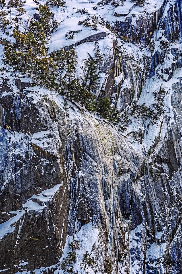 Snow covers the slopes as ice clings to the sheer granite rock face of the cliffsides high above Yosemite Valley in Yosemite National Park.