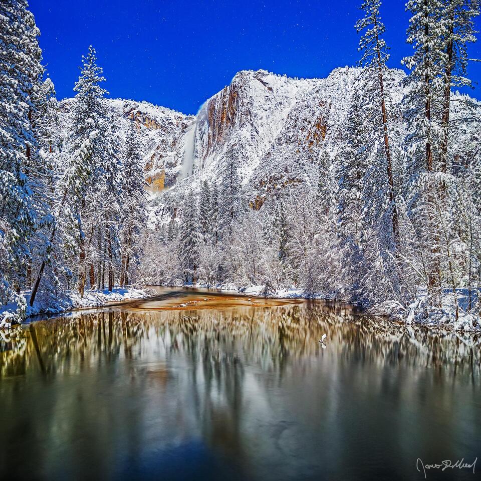 Moonlight illuminates Yosemite Falls as it tumbles 2425 feet over the snow covered granite cliffs above the Merced River and Yosemite Valley in the winter.