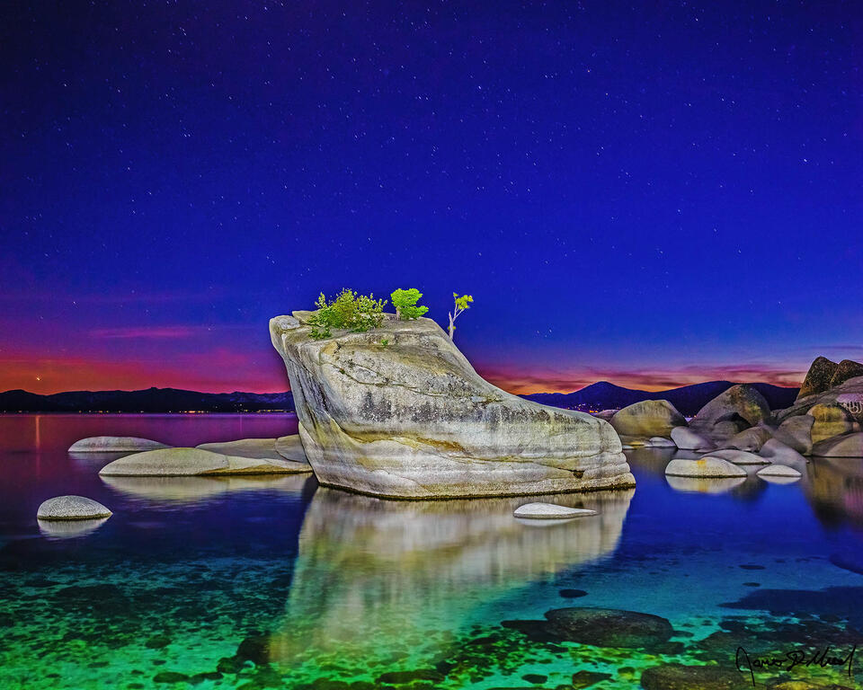 The last light of day hangs on along the horizon above Bonsai Rock and Lake Tahoe the darkness of night begins to set in at nautical dusk. 