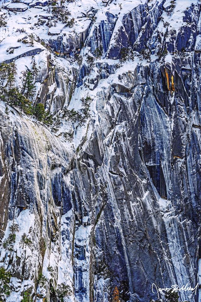 Snow covers the slopes as ice clings to the sheer granite rock face of the cliffsides high above Yosemite Valley in Yosemite National Park.
