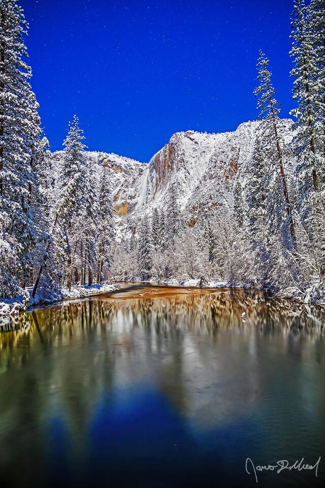 Moonlight illuminates Yosemite Falls as it tumbles 2425 feet over the snow covered granite cliffs above the Merced River and Yosemite Valley in the winter.