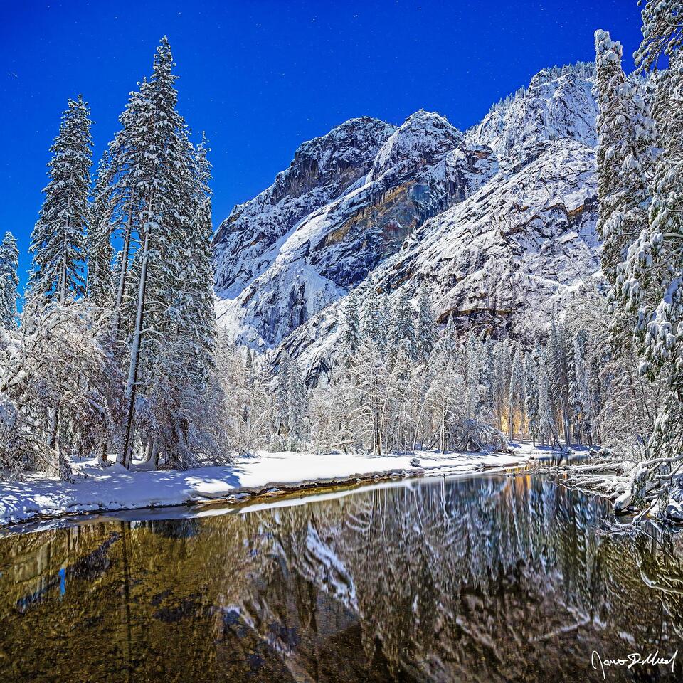Moonlight illuminates Glacier Point and snow covered Yosemite Valley in the winter, as the scene reflects in the crystal clear waters of the Merced River.
