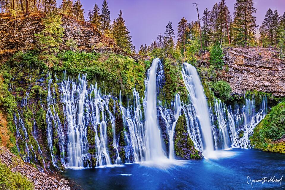 Burney Falls drops 129 feet over 250 feet of width as the sun sets through the trees above the falls.