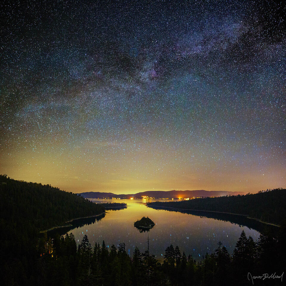 The Milky Way spiral arm streaks across the starlit skies above Lake Tahoe and Emerald Bay while the stars reflect in the waters of Emerald Bay below.