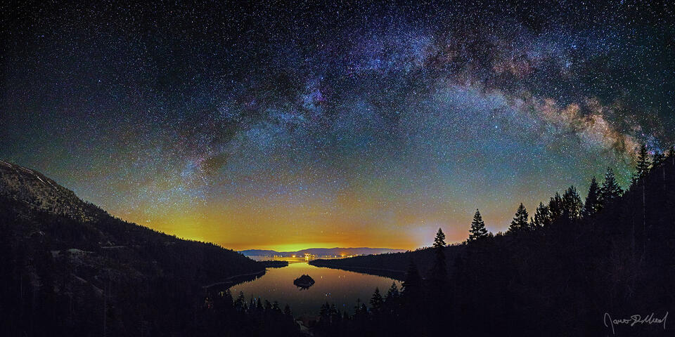 The Milky Way Arch stretches across the night sky over the Sierra Nevada Mountains and the waters of Emerald Bay and Lake Tahoe in California.
