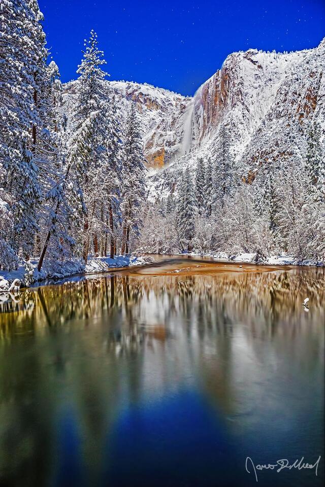 Moonlight illuminates Yosemite Falls as it tumbles 2425 feet over the snow covered granite cliffs above the Merced River and Yosemite Valley in the winter.