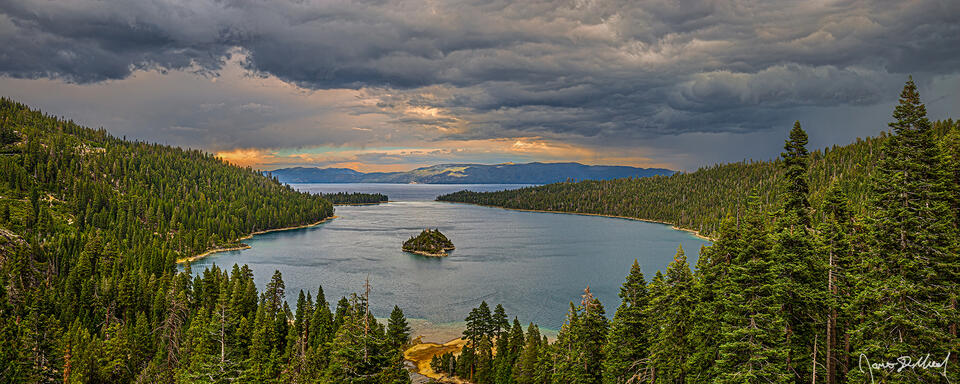Storm clouds cover the skies above Emerald Bay and Lake Tahoe as sunlight illuminates the cloud breaks along the horizon and overhead