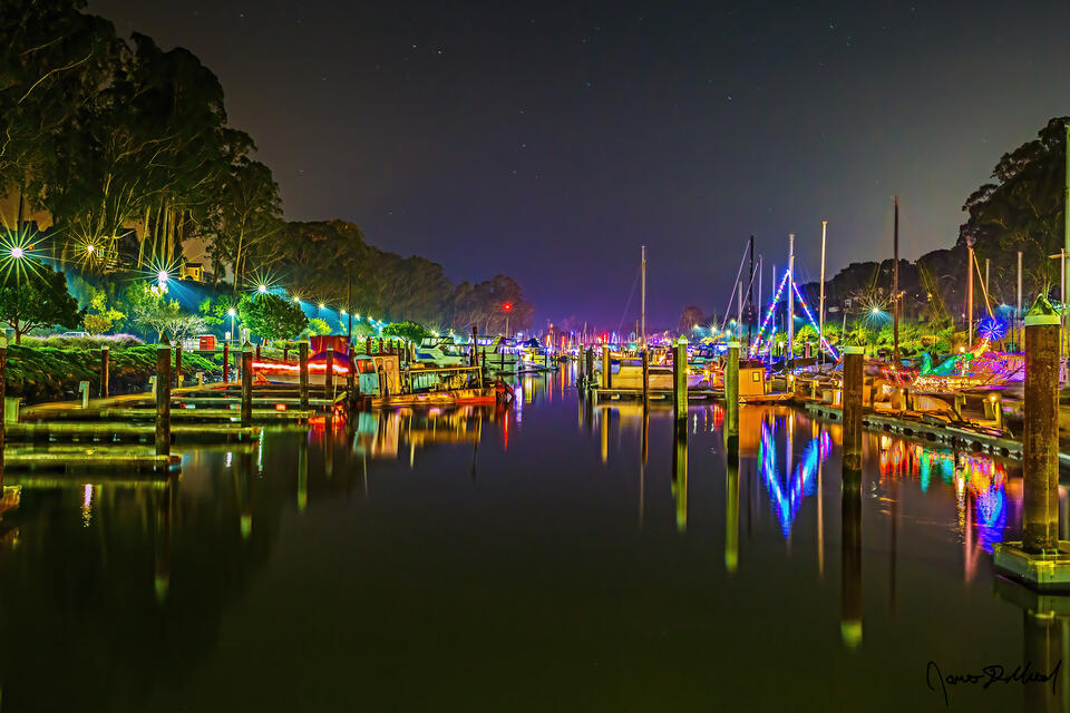 Christmas lights adorn the boats of Santa Cruz Harbor as the scene reflects in the still waters at night.