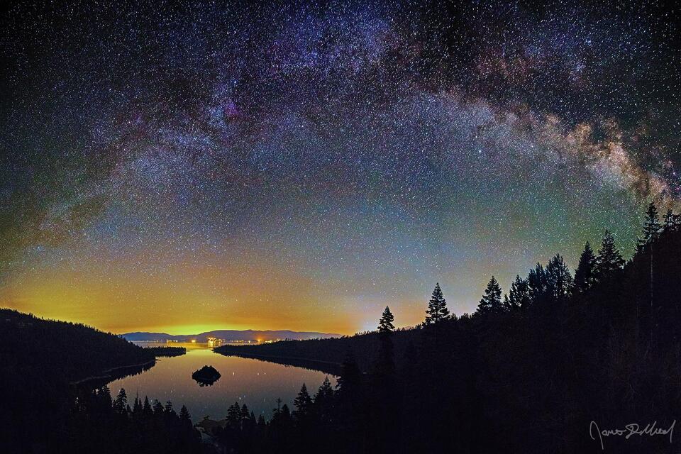 The Milky Way Arch stretches across the night sky over the Sierra Nevada Mountains and the waters of Emerald Bay and Lake Tahoe in California.
