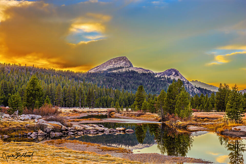Sunset lights the clouds above Fairview Dome, the Tuolumne River and Tuolumne Meadows as the granite peaks reflect in the still waters of the river.