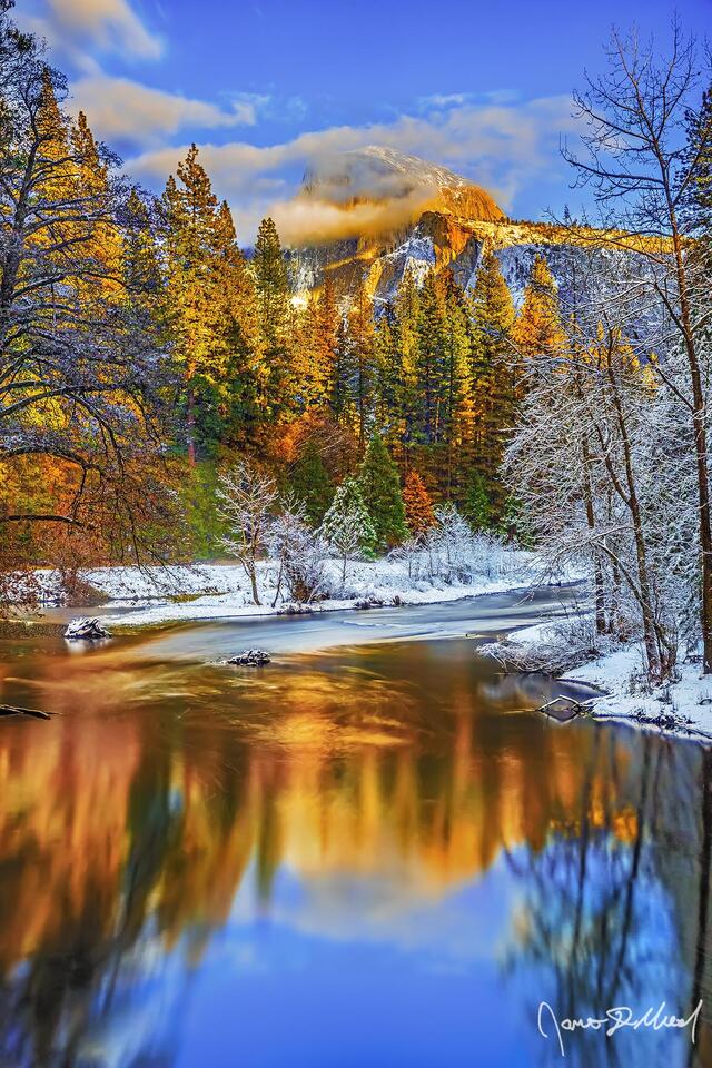 Enveloped by wispy clouds, Half Dome and the trees of Yosemite Valley stand bathed in the golden glow of winter sunset as they reflect in the Merced River.
