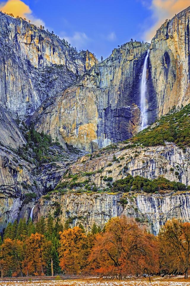 The setting sun casts a golden glow in the clouds above Yosemite Falls in the fall as it plunges 2,425 feet over the granite cliffs into Yosemite Valley.