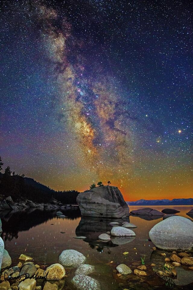 The Milky Way rises above Bonsai Rock and the still reflections in waters of Lake Tahoe as meteors from the Aquariids meteor shower streak across the night sky.