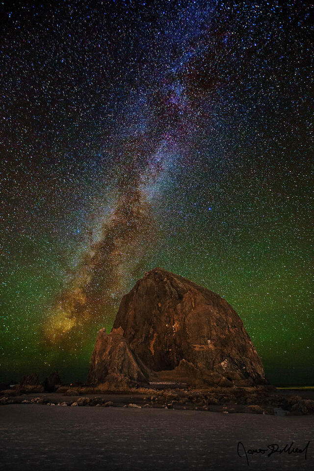 The Milky Way rises over Haystack Rock on the Northern Oregon Coast. Green and yellow airglow illuminates the night sky over Cannon Beach.