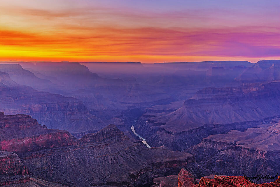 Haze from a prescribed burn envelopes the Grand Canyon as sunset produces a brilliant ray of sunlight through the haze in the canyon.