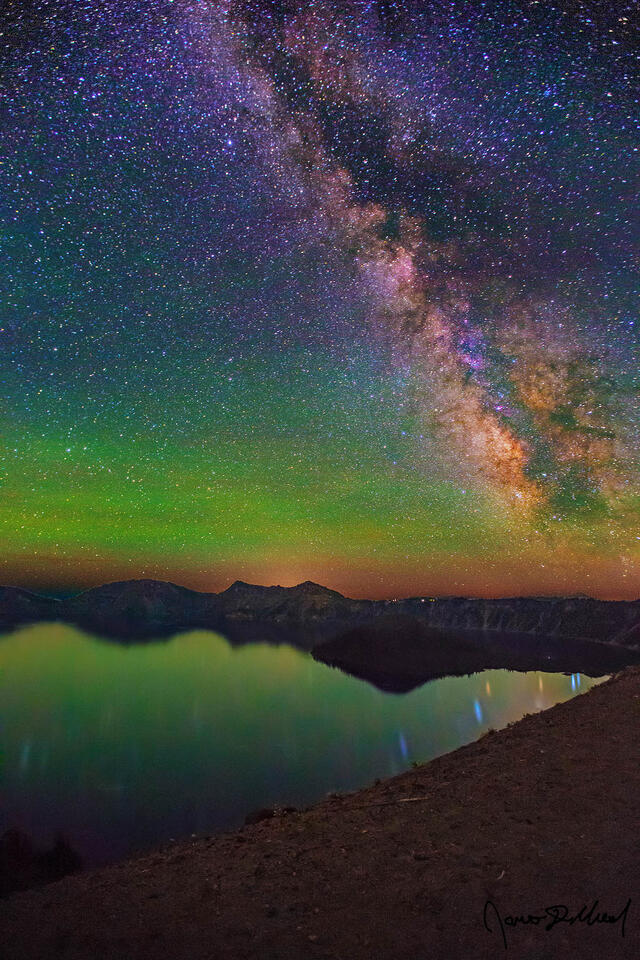 The Milky Way rises over Crater Lake and Wizard Island as the green airglow softly illuminates the dark night skies above.