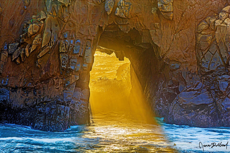 The setting sun creates a beam of light through Keyhole Arch on Pfeiffer Beach in Big Sur, California.