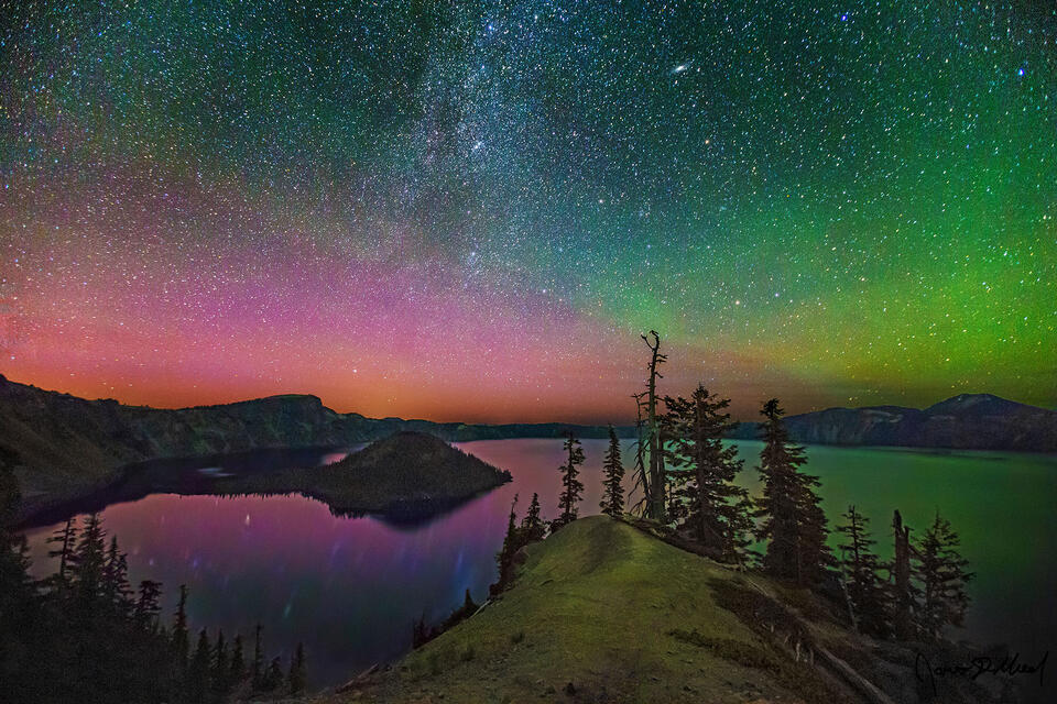 Magentas and greens of the Aurora Borealis light up the skies above Crater Lake and Wizard Island as the spiral arm of the Milky Way rises into the night sky.