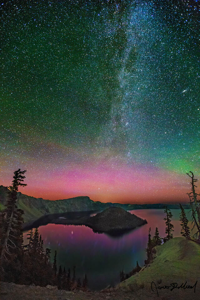 Magentas and greens of the Aurora Borealis light up the skies above Crater Lake and Wizard Island as the spiral arm of the Milky Way rises into the night sky.