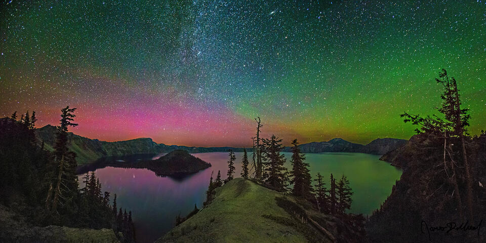 Magentas and greens of the Aurora Borealis light up the skies above Crater Lake and Wizard Island as the spiral arm of the Milky Way rises into the night sky.