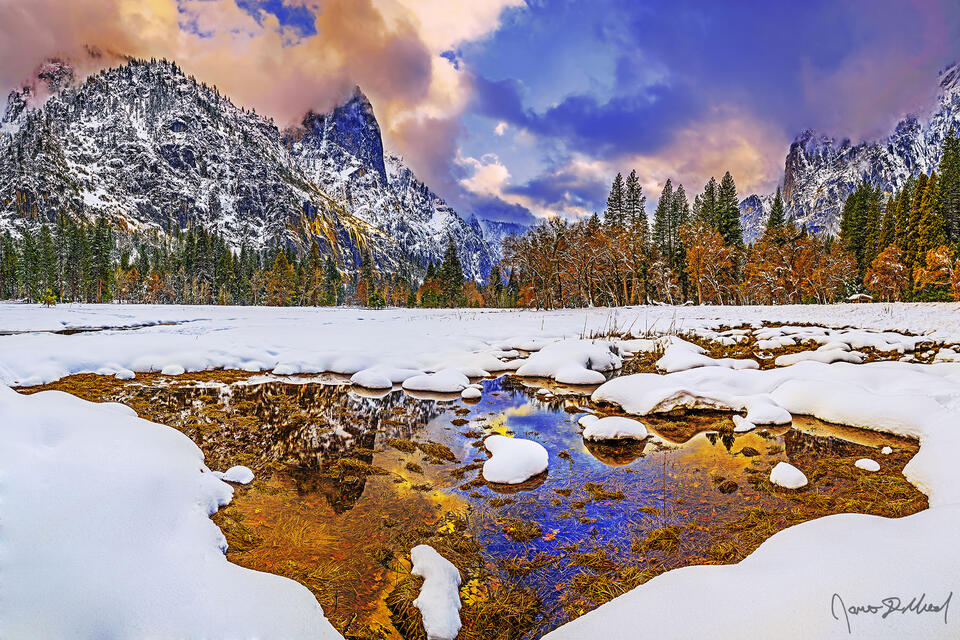 Sunset lights the skies above as the setting sun casts a warm glow on the slopes of Sentinel Rock high above Cook's Meadow and snow covered Yosemite Valley. 