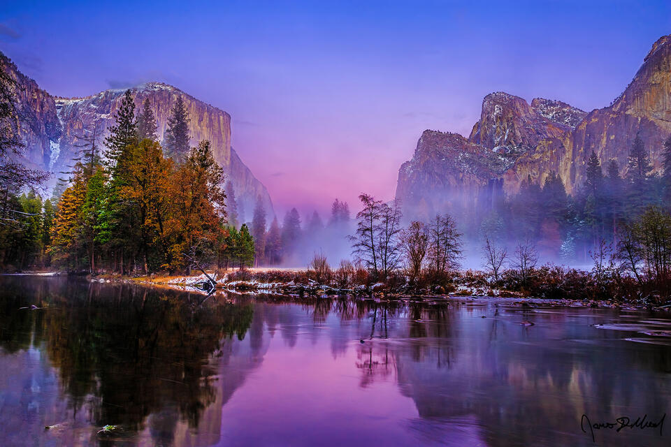 Alpenglow illuminates the skies above El Capitan and Cathedral Rocks as they rise up from a layer of mist and fog, reflecting in the water of the Merced River.