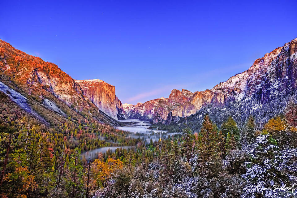 El Capitan, Half Dome & Cathedral Rocks illuminate with the last light of day as dusk nears. Fog rolls into the valley as snow begins to blanket the cliff tops.