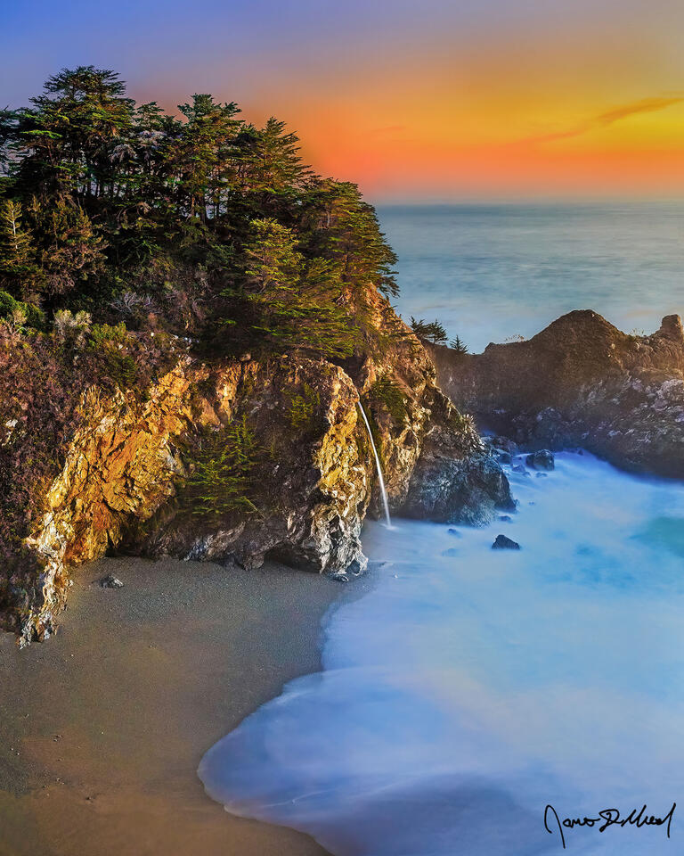 McWay Falls drops straight over the cliffs and directly into the Pacific Ocean at sunset as waves in the Pacific Ocean crash up into McWay Cove.
