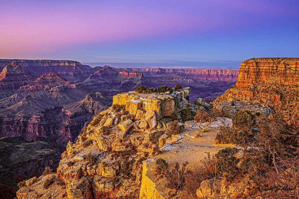 The warm glow of sunset bathes the buttes and temples of the Grand Canyon at sunset as the pastel colors of the Belt of Venus illuminate the skies above.