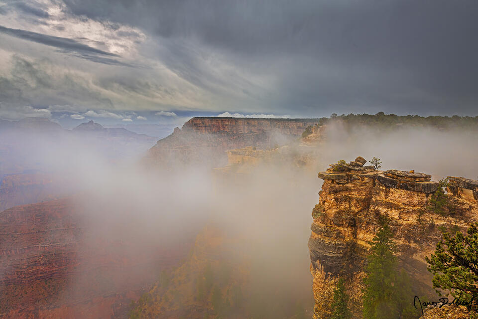 A temperature inversion (thermal inversion, cloud inversion) creates a rare sight as clouds fill the Grand Canyon while storm clouds line the skies high above.