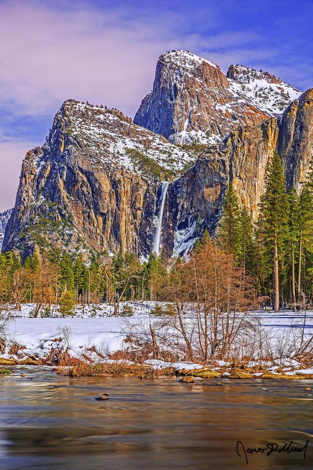 Sunset brings colors to the sky above the Merced River and Cathedral Rocks as Bridalveil Fall tumbles over the cliffs and towards snow covered Yosemite Valley