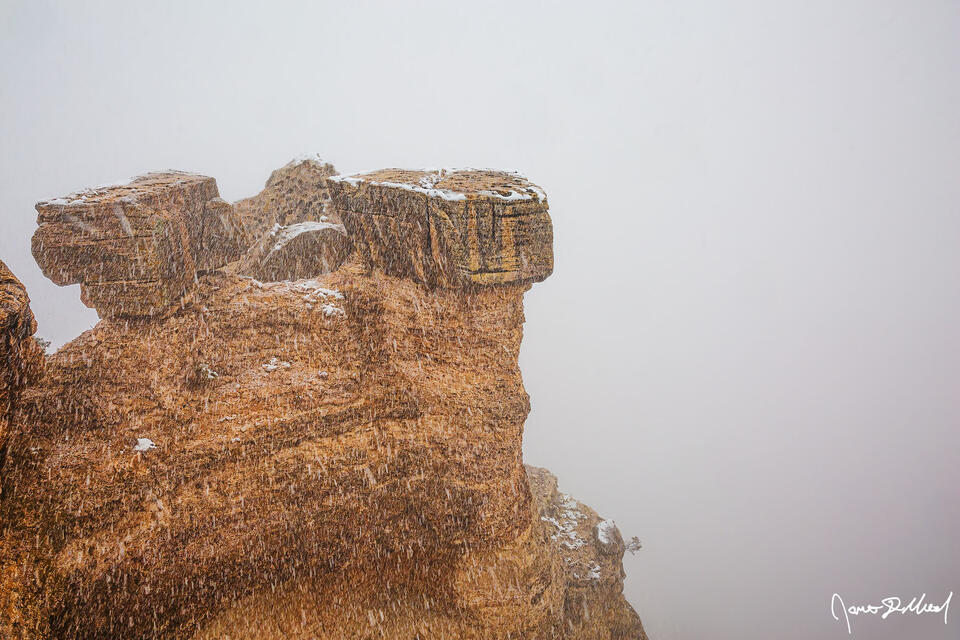 A thermal inversion during a winter snow storm covers the grand canyon in clouds and fog as a lone formation rises up out of the clouds as snow falls.