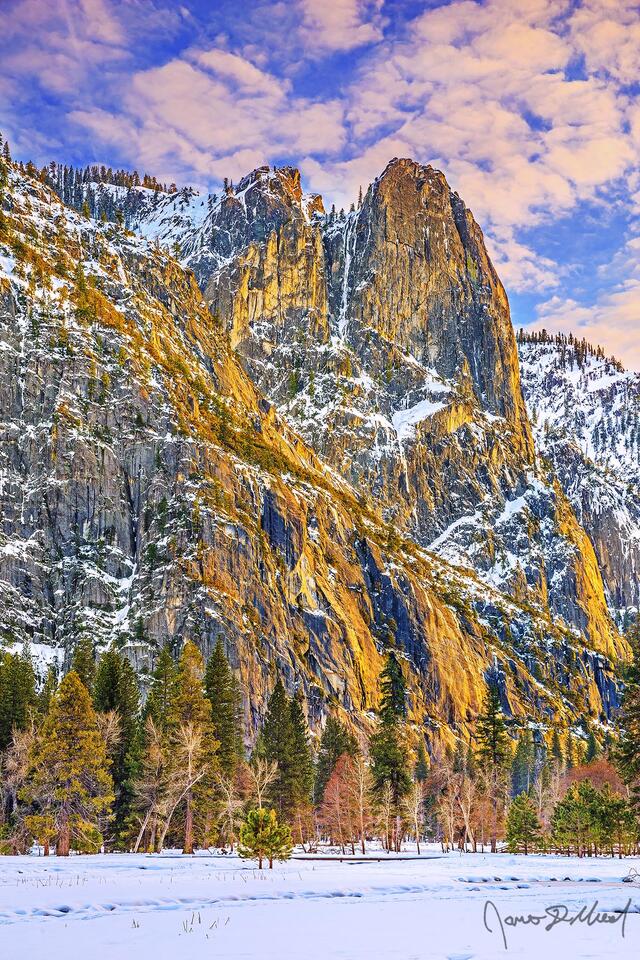 Sunset lights the skies above as the setting sun casts a warm glow on the slopes of Sentinel Rock high snow covered above Cook's Meadow and Yosemite Valley.