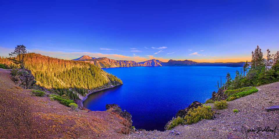 The setting sun casts a golden hue over the rim above the Sapphire blue waters of Crater Lake as Cleetwood Cove slips into the shade.