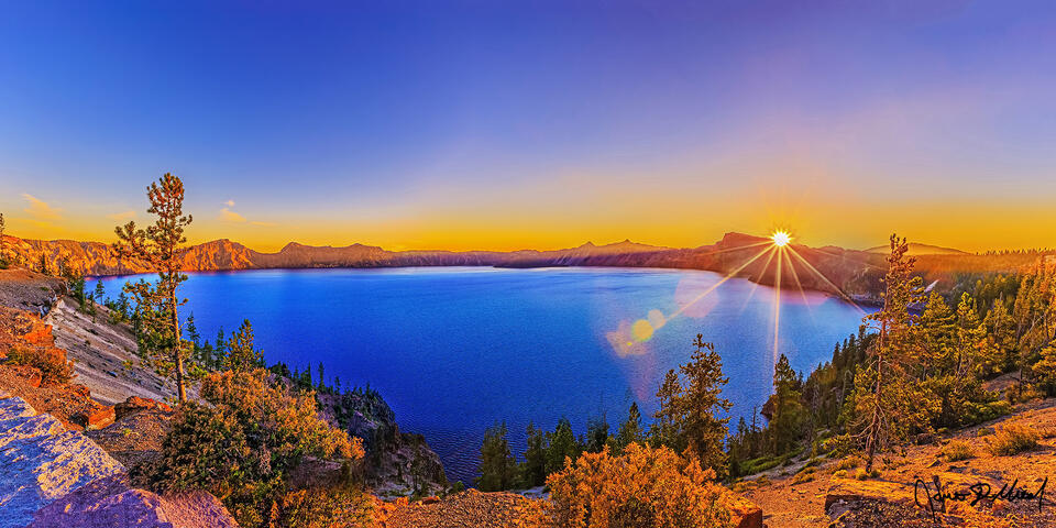 The setting sun creates a sun star as it lights up Crater Lake, Oregon's only National Park, while casting a warm glow over Palisade Point