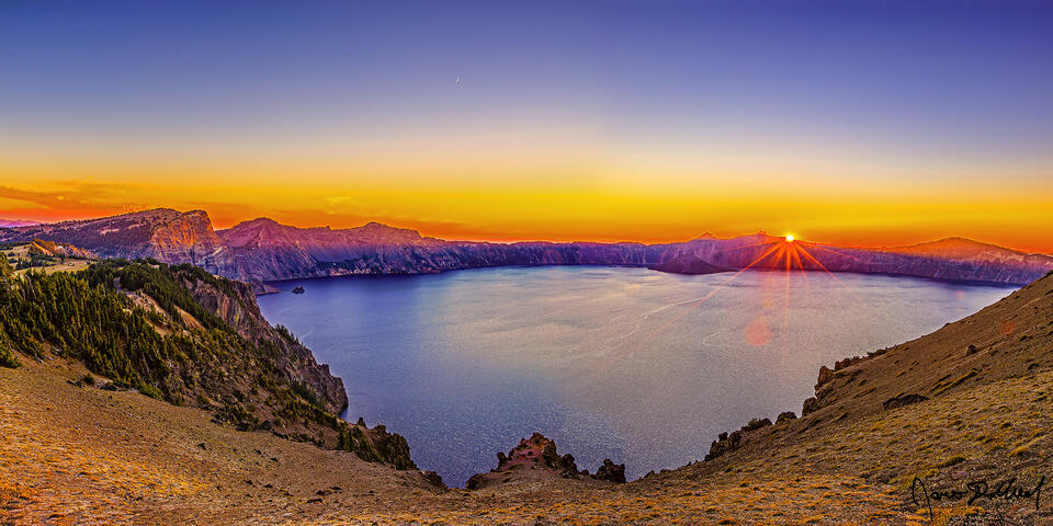 Sunset reflects off the waters of Crater Lake above Cloudcap Overlook as the setting sun stars off the edge of the caldera rim.