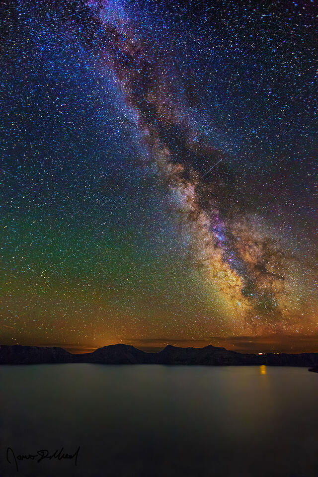 The Milky Way rises high into the night skies above Crater Lake as airglow faintly illuminates the night sky above.