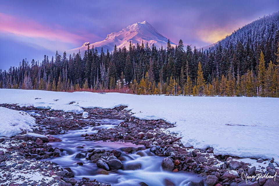 Long after sunset as nautical twilight sets in, a glacial river meanders through a frozen blanket of snow while alpenglow sets fire to the slopes of Mount Hood.