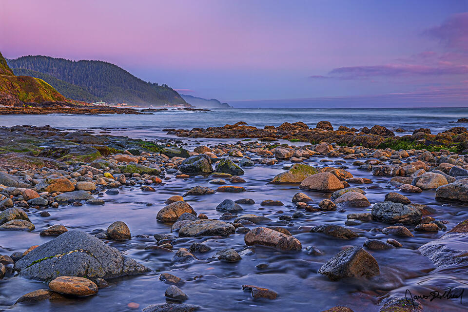 Pastel colors at sunset illuminate the skies above the Coastal Headlands of the Oregon Coast as a creek flows directly into the Pacific Ocean.