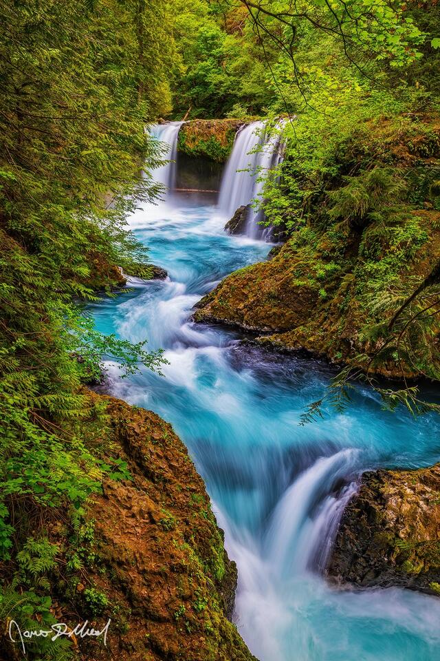 Surrounded by trees hidden deep in the forest, turquoise glacial water of Spirit Falls flows over the ledge into the pool and through the narrow channel